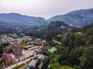An aerial view of the mountain town of Maubisse in Ainaro, Timor-Leste. A historic old church stands at the center of the village, surrounded by the vast green highland landscape.