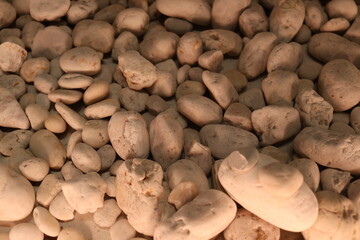 Close up view of numerous rounded smooth pale cream colored river stones filling the frame