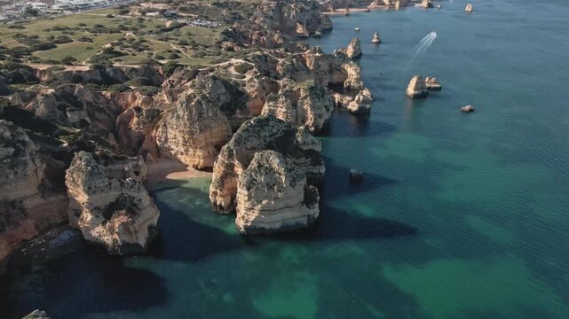 Aerial drone performs a dynamic helix orbit, circling high above the dramatic golden limestone stacks and hidden coves along the coast near Lagos, Portugal.