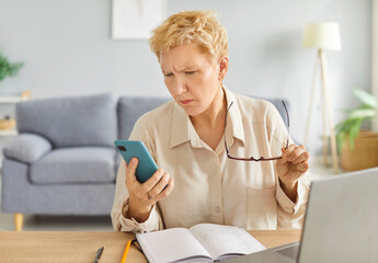 Shocked in worry, concerned mature woman at home holding phone, staring at smartphone screen in bad surprise, getting stress, financial problems, money stealing, risk, reading angry message