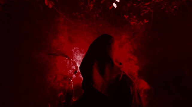 Classic grim reaper in a cloak holding a scythe with smoke or mysterious fog and backlighting in a cemetery graveyard. Death looming over a graveyard. Halloween or classic horror. Fire red hellish.