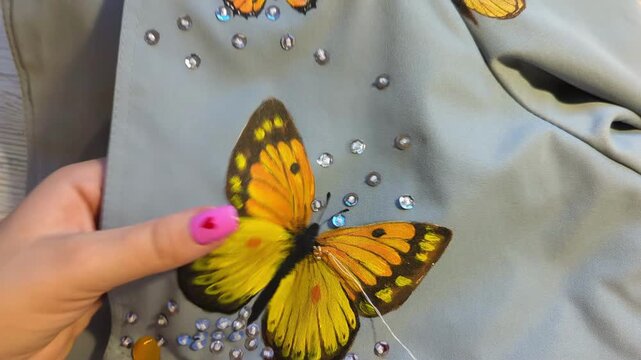 Detailed macro shot of a needle and thread creating a handmade embroidered butterfly pattern decorated with sequins. Creative hobby. Female designer sewing.