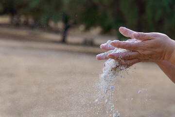 Hands releasing loose sand, grains falling through aged fingers to symbolize time, fragility, impermanence, and letting go