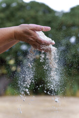 Hands holding and sifting white flour, with particles falling through fingers, demonstrating baking preparation