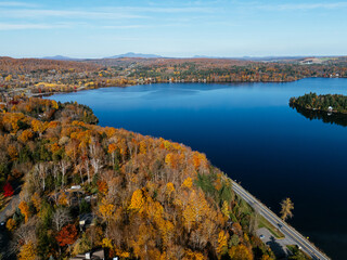 Drone aerial of a winding lakeside road with residential buildings and autumn forest in Canada. g.