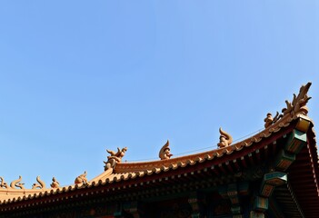 Fototapeta premium Traditional Asian architecture with ornate roof design featuring decorative dragon figures against a clear blue sky in serene cultural setting