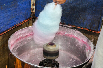 The process of making cotton candy using a machine. A man's hands are making colorful cotton candy.