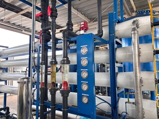 Industrial water treatment machinery featuring multiple horizontal Reverse Osmosis (RO) membrane vessels or filter housings. The system includes a blue control panel with pressure gauges and black PVC