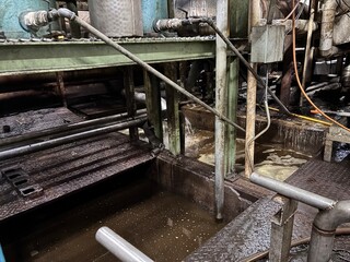 Grungy industrial platform submerged in contaminated brown water, showing slippery metal grating, exposed pipes, and sludge overflow, highlighting poor workplace safety and environmental hazard 