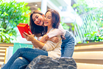 Happy Asian daughter give pink gift box to mother while shopping together at shopping mall. Senior mom and adult child girl celebration birthday party or mother's day. Happy Family relationship.