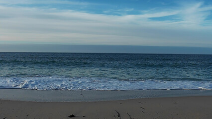 coastal waves scene, turquoise surf colliding with dark cliffs beneath cloudy sky at shoreline