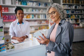 Smiling senior woman using app on smart phone while buying in pharmacy.