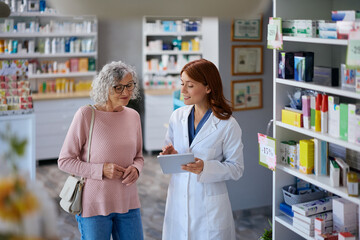 Happy pharmacist and senior woman using digital tablet in pharmacy.