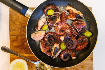 Fried octopus in olive oil with olives and wine served in a pan