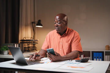 Senior man analyzing finance data using laptop and smartphone