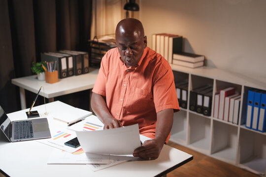 Mature black man analyzing financial documents at home office - Powered by Adobe
