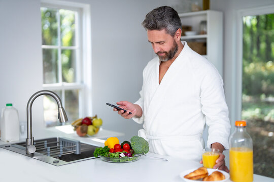 Man eats breakfast in the kitchen on morning. Man enjoys a healthy meal at the kitchen table. Middle aged man eats cereal and fruit in the kitchen during morning hours. Man eats vegetables for lunch. - Powered by Adobe