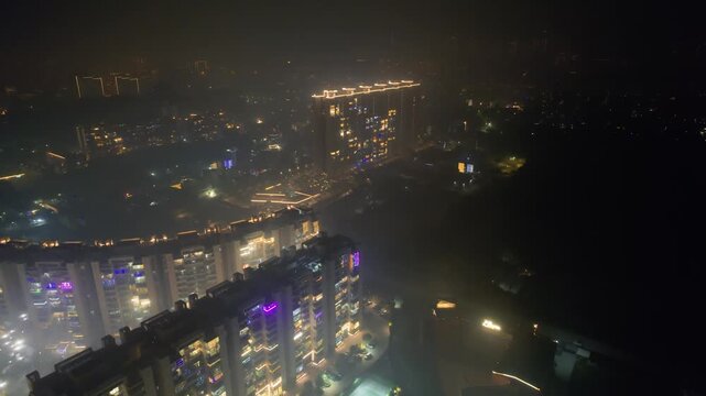 aerial drone descending over brightly lit and decorated buildings for diwali with fireworks going all around with delhi cityscape in distance with smoke smog fog pollution over Delhi, Gurgaon, Noida