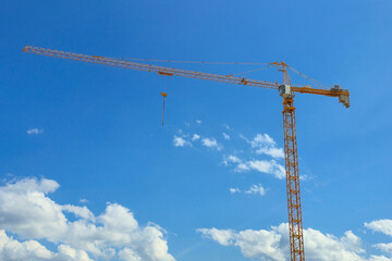 A crane is standing tall in the sky above a blue sky. The crane is yellow and has a black and white...
