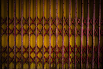 Close-up of red accordion-style metal gate over yellow corrugated surface. Ideal for industrial, architectural, or geometric design themes.