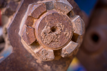 Close-up of a large tractor bolt covered in mud and rust. The worn surface and hexagonal shape highlight heavy-duty use in agricultural or mechanical environments.