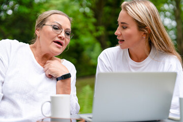 Women discussing ideas outdoors while using a laptop in a green park setting during a sunny day