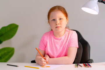 Young girl focused on drawing with colored pencils in a bright room during the afternoon
