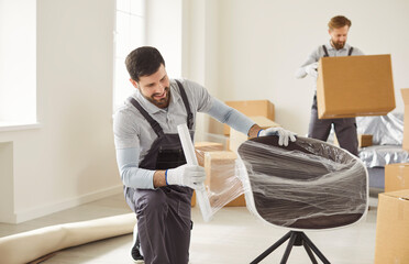 Movers wrapping chair for relocation and delivery. They apply plastic wrap and tape for protection, packing boxes, and coordinate logistics for transport. Concept packing service with care.
