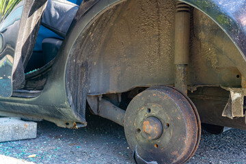 Rusty brake drum and suspension of a car without a wheel after a road collision, visible interior and glass fragments on asphalt beneath the wheel arch