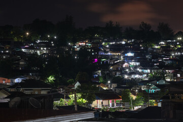Fototapeta premium Night view of a dense, tiered residential neighborhood on a hill, illuminated by streetlights and house lights with beautiful starburst effects.