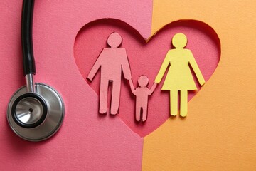 Family health concept.  A stethoscope rests atop a divided background of pink and orange cardstock.  A heart-shaped cutout reveals paper cutouts of a family?mother, father, and child?holding hands