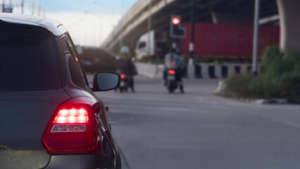 Rear side of dark car turn on brake light on the road. Car park at the intersection with a red traffic light. There are cars going straight across. Under the overpass at evening.