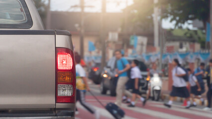 Rear side of car with turn on brake light on the road. Road crossing point with blurry image of students passing by.  Stop to pass for safety reasons. Morning time in the city of Thailand.