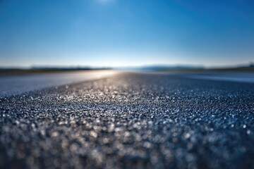 Close-up of asphalt road, dew-kissed, leading to distant horizon under bright sun