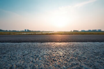 Asphalt road edge at sunset.  Blurred cityscape and fields in the background.  Focus on the textured road surface