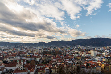 Obraz premium Panoramic Aerial View of Graz Austria Cityscape with Red Roofs and Hills under Dramatic Cloudy Sky