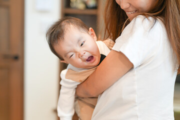 A woman is holding a baby in her arms. The baby is smiling and making a funny face. The woman is smiling back at the baby, creating a warm and loving atmosphere
