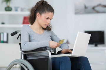 girl in wheelchair using laptop and holding bank card