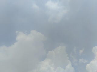Vast, calming blue-gray sky partially obscured by soft, bright cumulus clouds, with a subtle contrast of m odern power lines hinting at the urban or rural edge below.