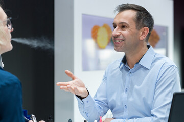 woman trying vaporizer and exhaling towards salesman