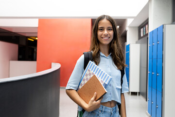 Smiling student girl holding books in school hallway