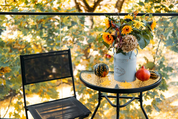 Simple autumn balcony setup with floral centerpiece in a vintage can beside gourds and a mesh chair...