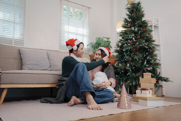Obraz premium Happy couple wearing Santa hats exchanging Christmas gifts at home, celebrating holiday season with joy and warmth by the Christmas tree.