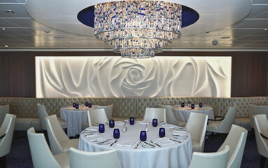 Formal and elegant ocean view a la carte dining room restaurant onboard luxury cruiseship cruise ship liner with set tables in white and blue Art Deco interior design style ceiling ambient lighting