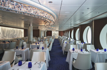 Formal and elegant ocean view a la carte dining room restaurant onboard luxury cruiseship cruise ship liner with set tables in white and blue Art Deco interior design style ceiling ambient lighting