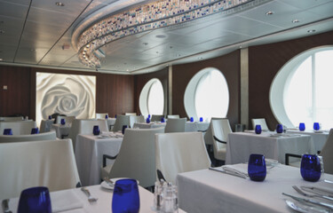 Formal and elegant ocean view a la carte dining room restaurant onboard luxury cruiseship cruise ship liner with set tables in white and blue Art Deco interior design style ceiling ambient lighting