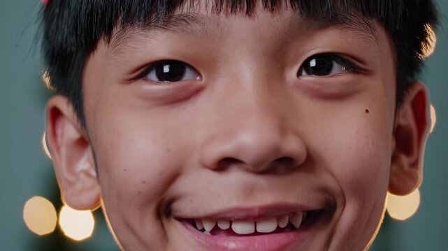 Close-up of joyful boy smiling in festive atmosphere. Bright lights create warm holiday spirit. Innocent happiness and celebration captured in children's joyful expression.