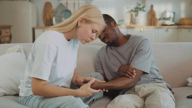 Careful woman stroking broken arm of her beloved boyfriend, man feel hard ache. Care and love in relationship, interracial marriage, african american and caucasian ethnicity, save health, stay healthy