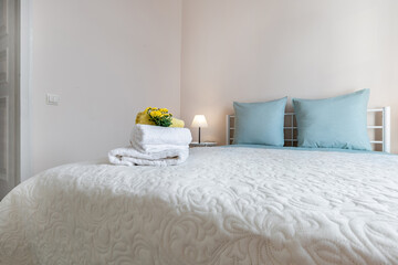 Bright Bedroom Interior with Blue Pillows and Fresh Towels on Bed