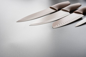 Modern pastel kitchen knives with silicone grips line the right on a silver gradient table; clean pro chef tools, color blades, wide copy space for text or menu design. Photo